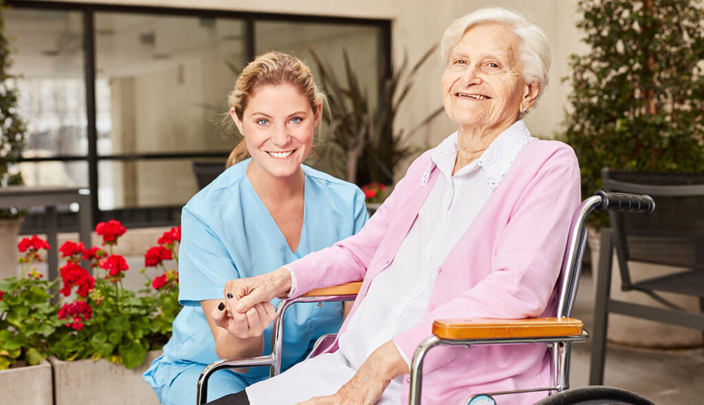 Home healthcare worker holds hands with elderly woman in wheelchair.