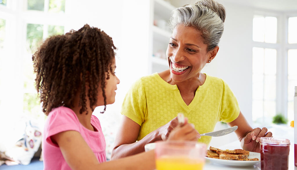 Grandmother eats breakfast with granddaughter at home.