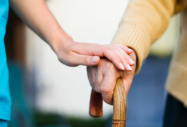 Home healthcare worker holds the hand of elderly person using a cane.